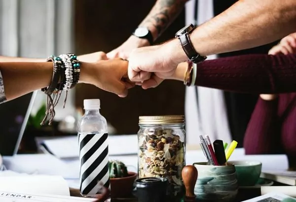 New Work e.V. – Mehrere Hände treffen sich in der Mitte eines Tisches zu einem gemeinsamen Fistbump. Symbol für Teamgeist, Zusammenarbeit und gemeinsames Wachstum in der modernen Arbeitswelt.